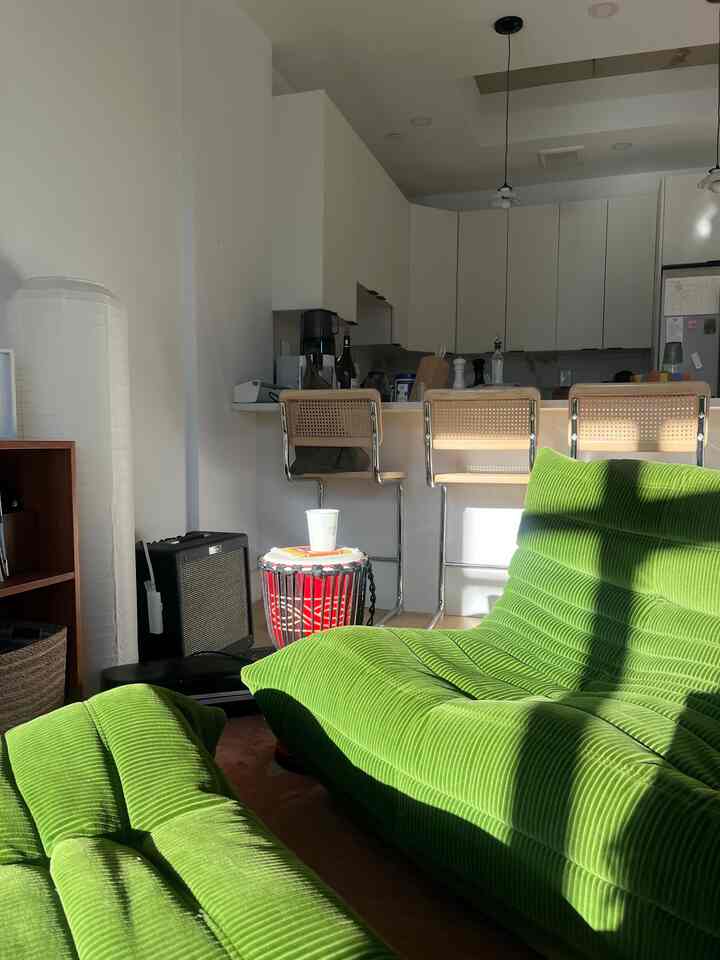 White and green toned living room and kitchen featuring green velvet ottomans and bar stools with bright natural ambiance