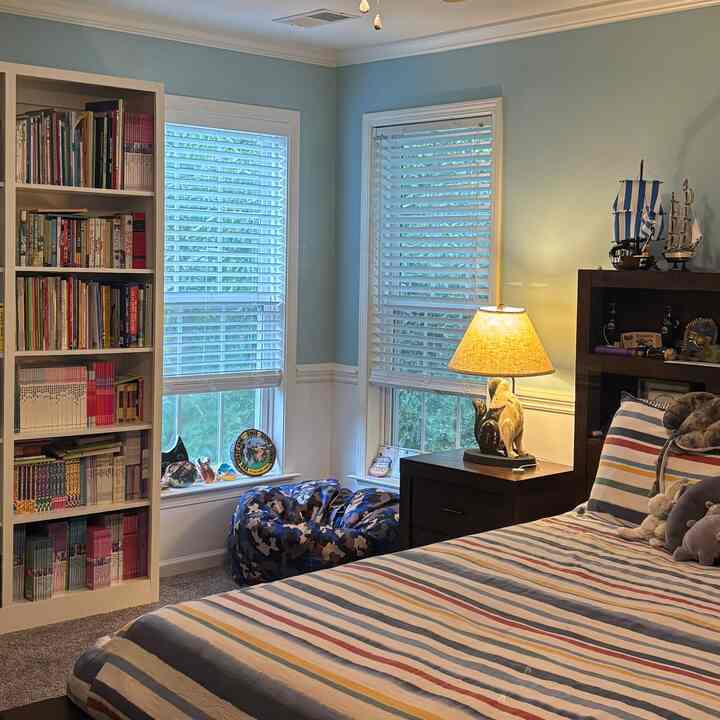 White and blue toned kids' bedroom featuring bookshelf, bean bag, and table lamp on nightstand with cozy atmosphere