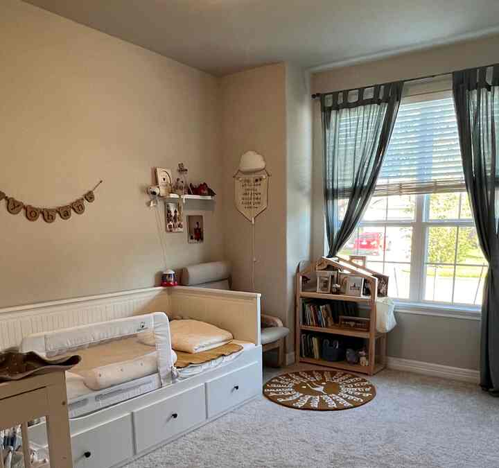 White and brown toned children's bedroom featuring a bed frame, bookshelf, and curtains with a cozy and clean atmosphere