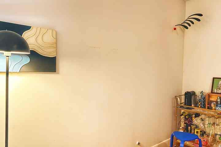 Cream-colored walls and white-toned living space featuring a bar cart, blue stool, floor lamp, and mobile for a cozy interior