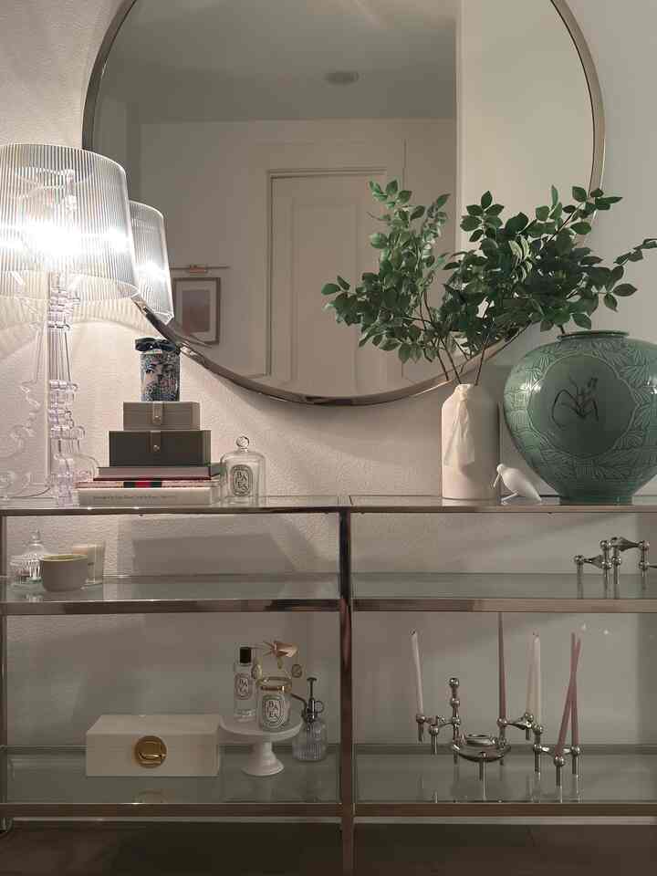 White-toned modern entrance space featuring a round mirror, natural greenery, candle holders, and metal shelving with a cozy ambiance