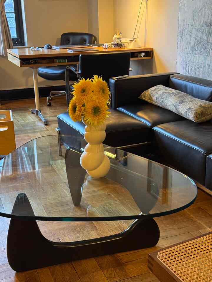 Wood tone floor and black leather sofa with glass-top Noguchi coffee table in a home office combined living room space