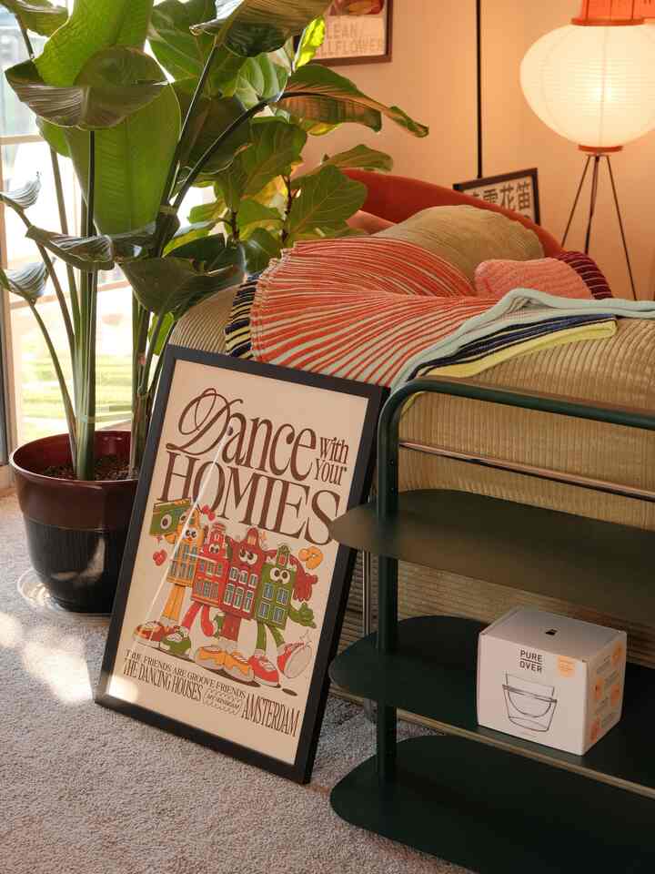 Warm-toned entrance space featuring beige bed, green plants, rug, and framed poster creating a cozy natural atmosphere