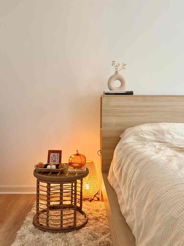 Beige and brown toned bedroom featuring a natural wood bed, wicker side table, and mood lighting creating a cozy atmosphere