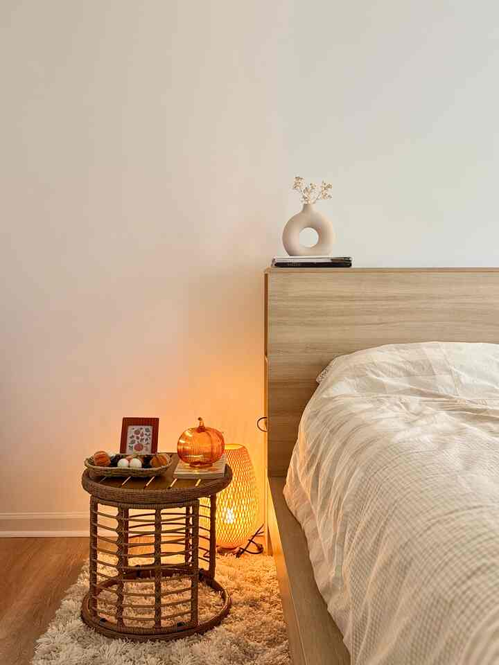 Beige-toned cozy bedroom featuring wooden bed and side table with orange LED glass pumpkin light creating warm atmosphere.