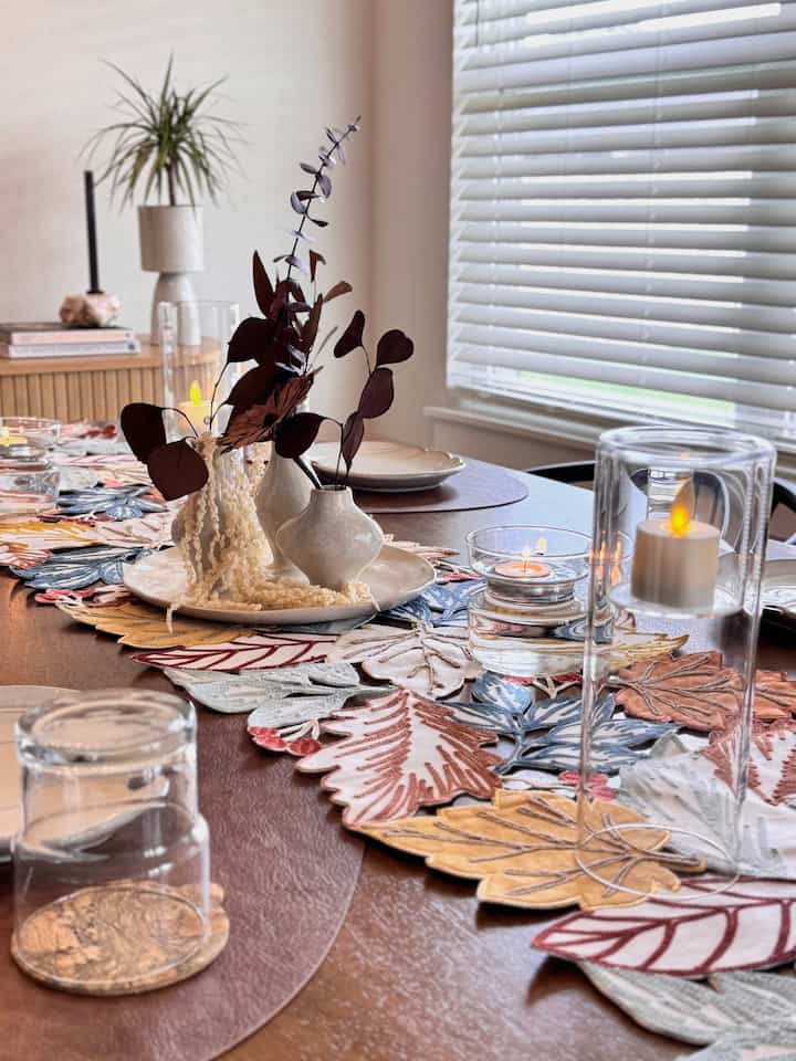 Brown toned dining table featuring a leaf-patterned table runner and candles creating a natural styled dining space