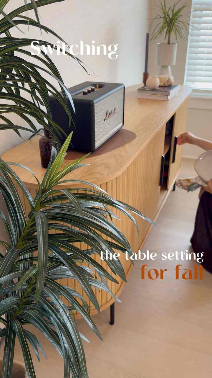 Wood tone sideboard and green plant in living room with cozy fall table setting atmosphere