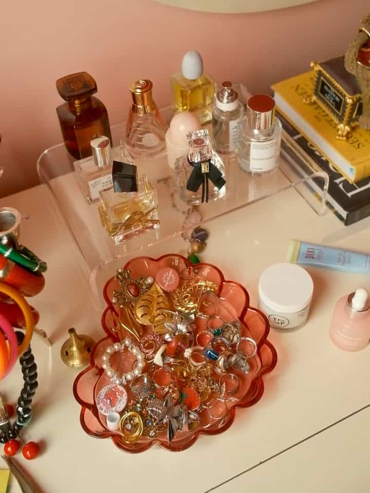 A cozy vanity space on a pink surface featuring gold decorative rings and a transparent acrylic stand