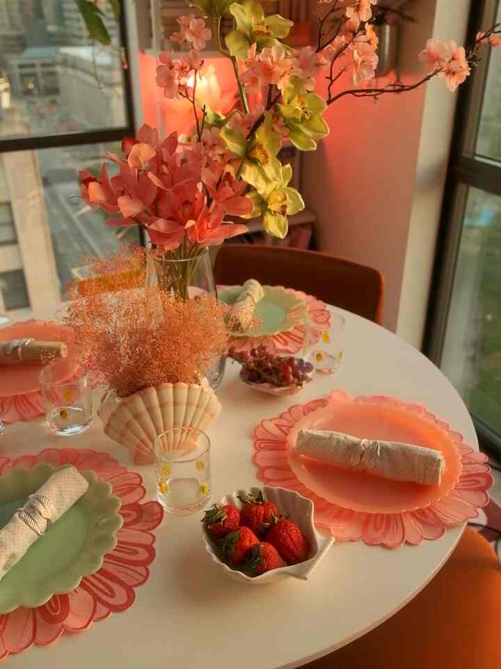 A natural toned dining room with a white round table featuring vases of flowers and pastel plates set for a cozy home party.