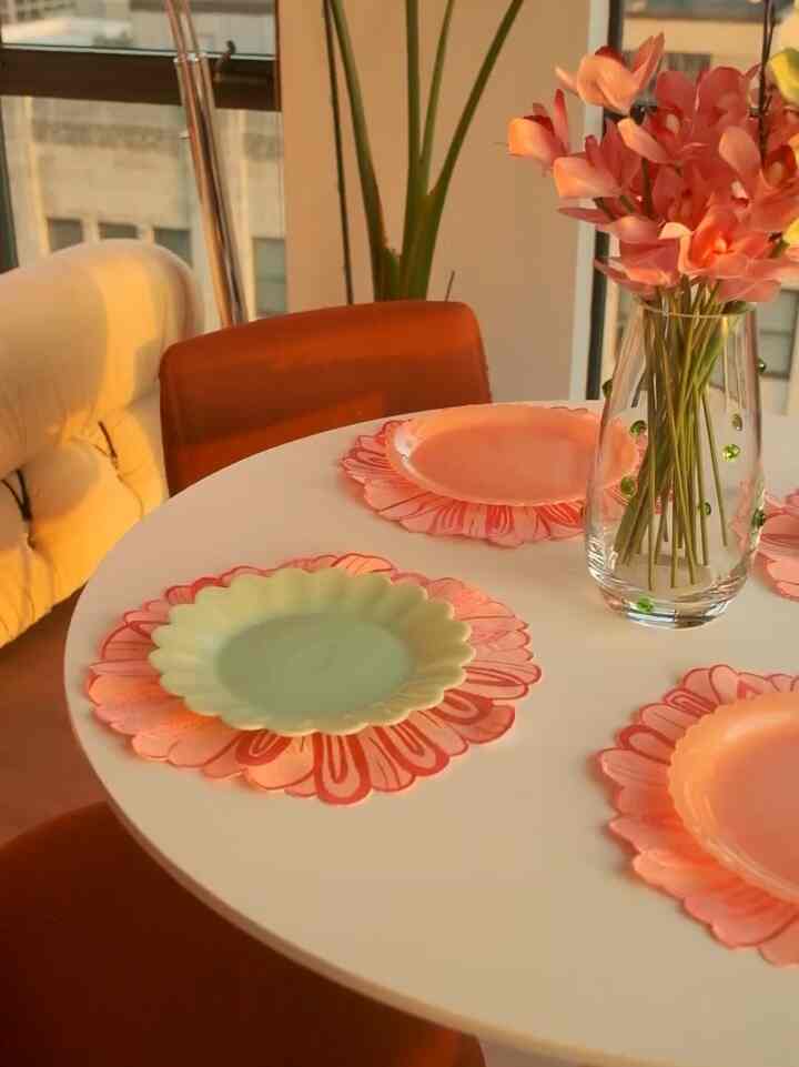 Warm sunlight illuminates a white round dining table with orange chairs and a flower vase, creating a cozy dining area
