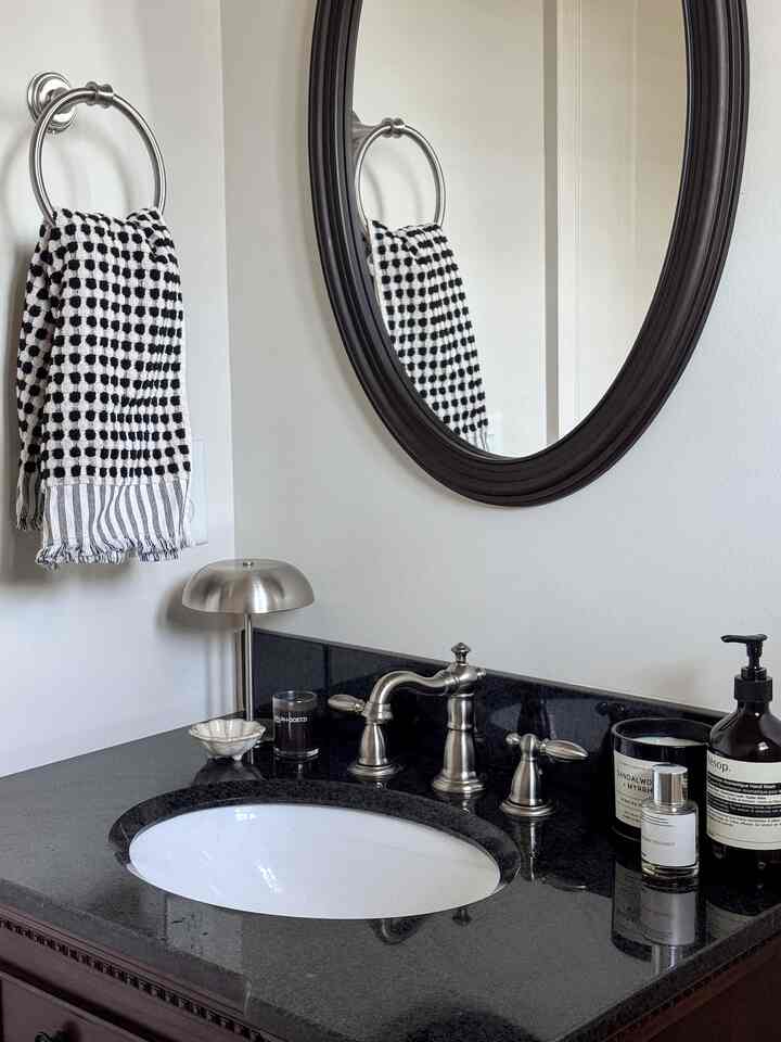 Monotone black and white powder room featuring an oval mirror, chrome faucet, and checkered towel in a neat setting