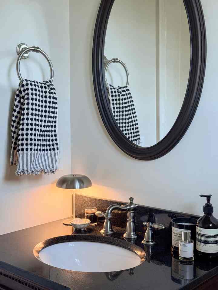 Modern black and white bathroom featuring black granite sink, metallic faucet, table lamp, and oval mirror creating a sleek atmosphere
