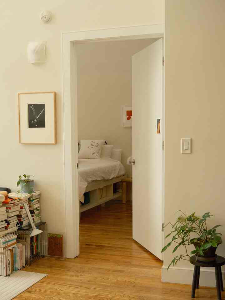 Natural-toned entrance area with white walls and wooden floor featuring a small bedroom, plants, and a bookshelf creating a cozy atmosphere