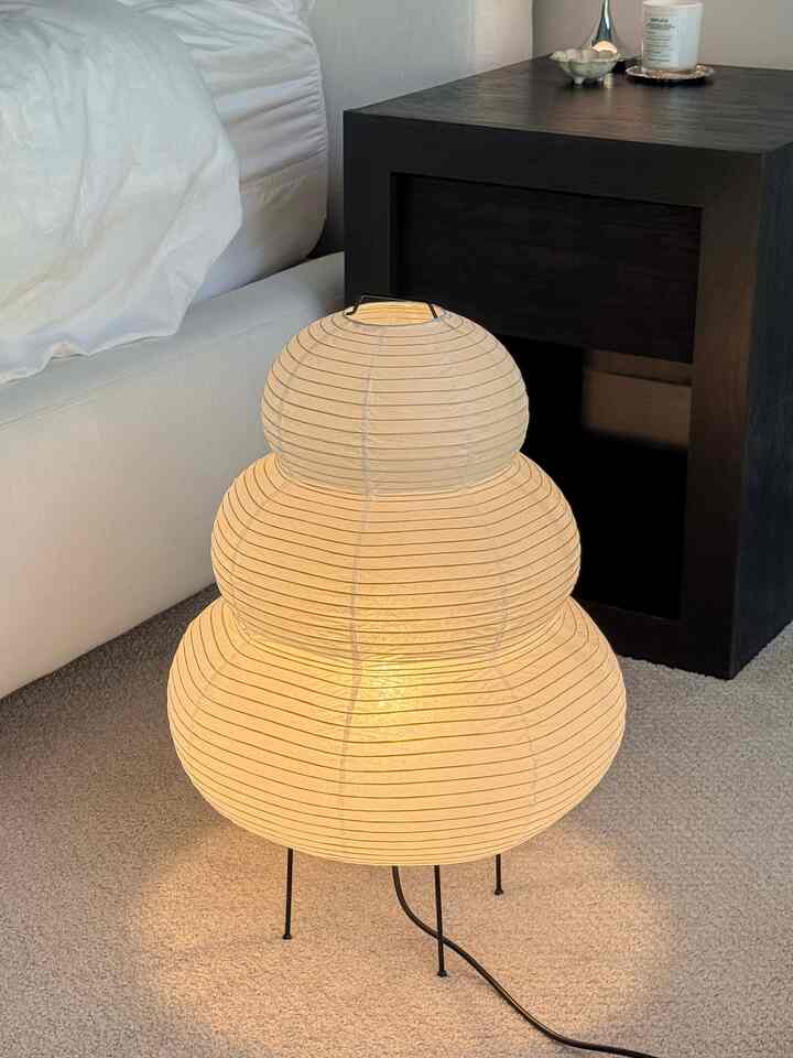 Natural-toned corner of a living room featuring a softly lit Noguchi paper floor lamp on a beige carpet