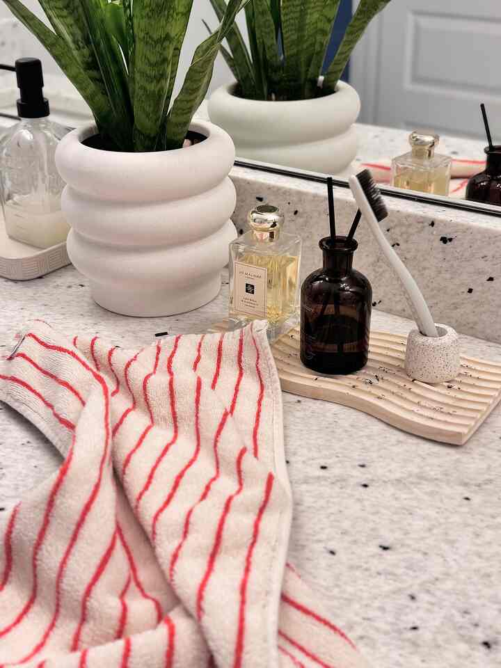 Gray and white bathroom vanity featuring a green plant, wooden tray with diffuser, and red-striped towel arranged neatly