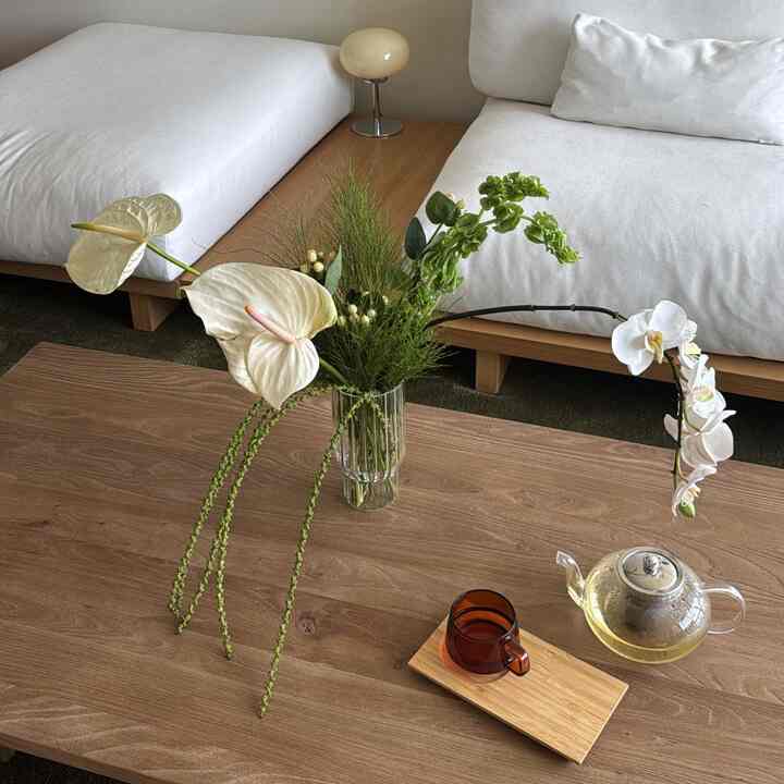 Natural wood-tone and white sofa living room featuring simple Ikebana floral arrangement and home cafe tea set on coffee table