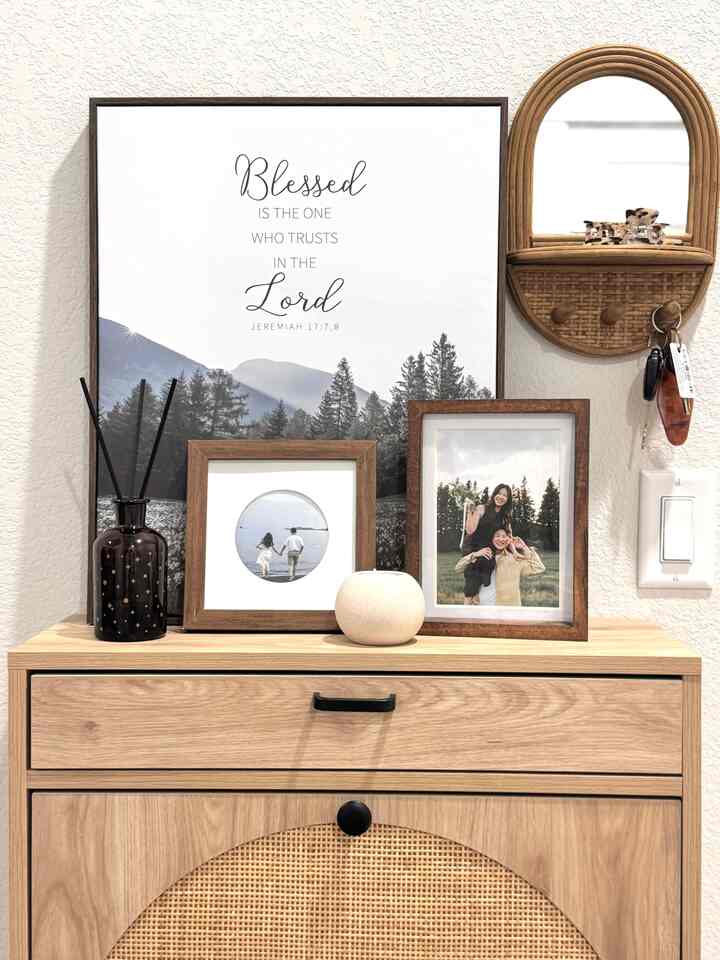 A simple and natural wall area featuring a wood-tone vanity and rattan mirror with decorative frames
