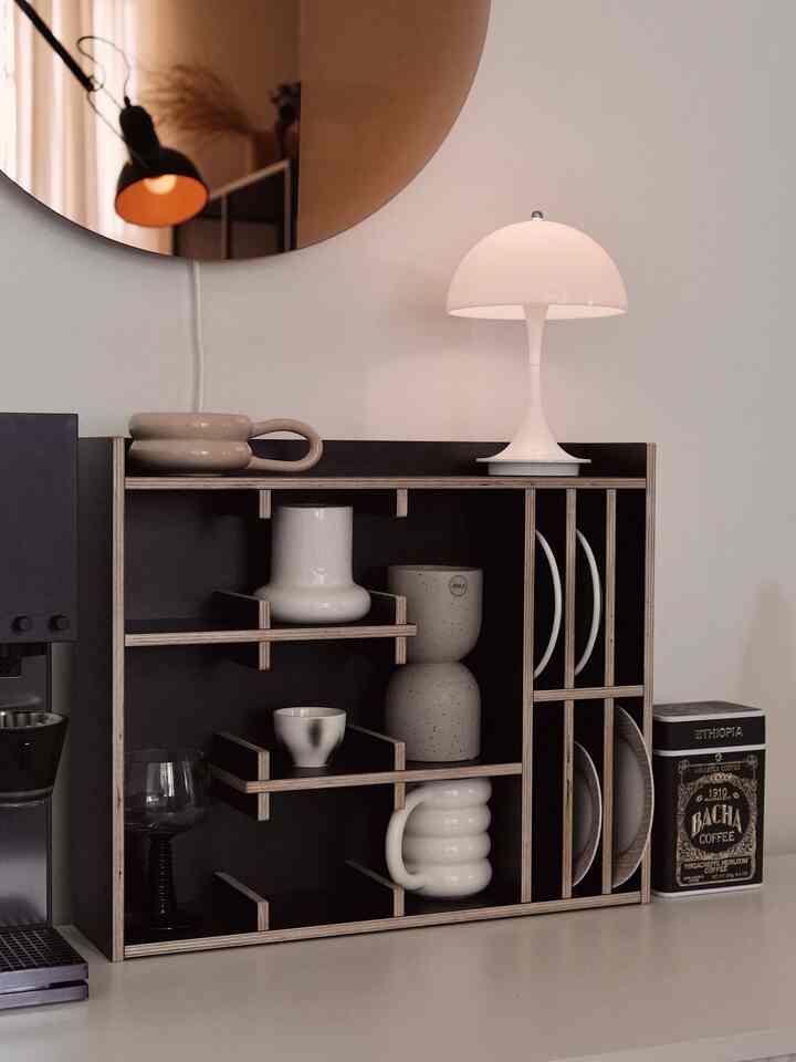 Ivory and black toned kitchen space featuring Pantella table lamp, mugs, plates, and coffee machine organized on a minimalist shelf.