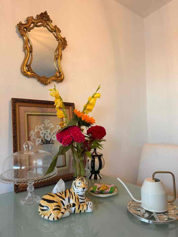 Ivory-toned wall and glass table featuring vase with vibrant flowers and ceramic tiger tissue cover in a cozy dining room space