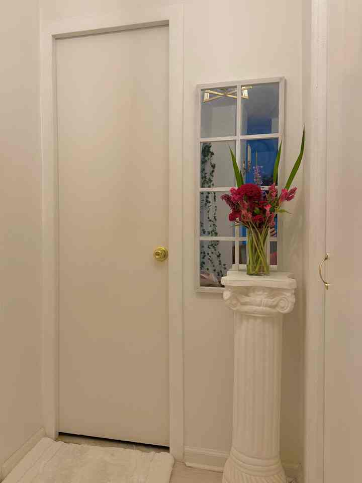 White-toned entrance space featuring a transparent vase with pink flowers placed on a white Corinthian column pedestal, showcasing a clean interior