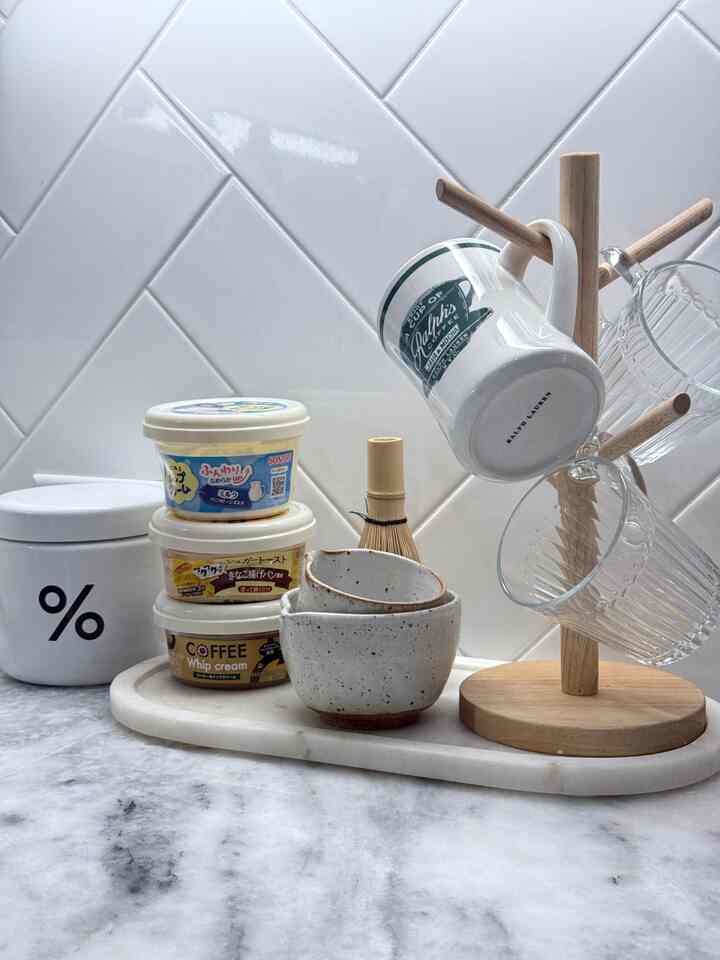 Clean kitchen home cafe space featuring white tiled wall, marble countertop with mugs, teacups, and a wooden mug rack