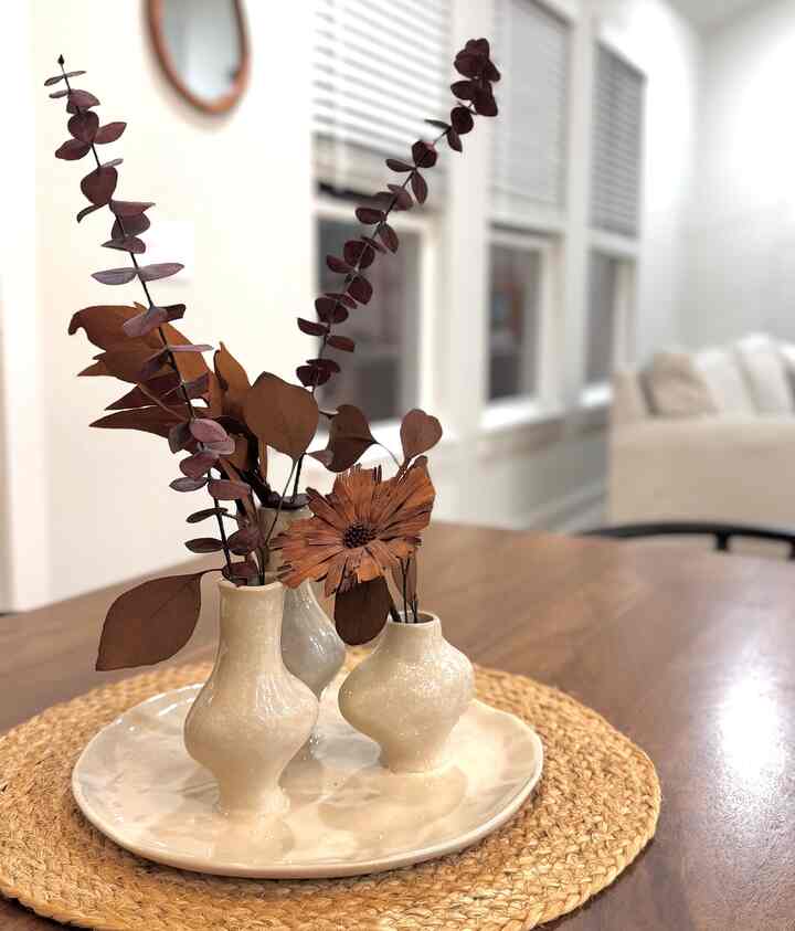 Natural-toned dining room featuring ivory ceramic vases with brown dried foliage on a wooden table creating a warm ambiance