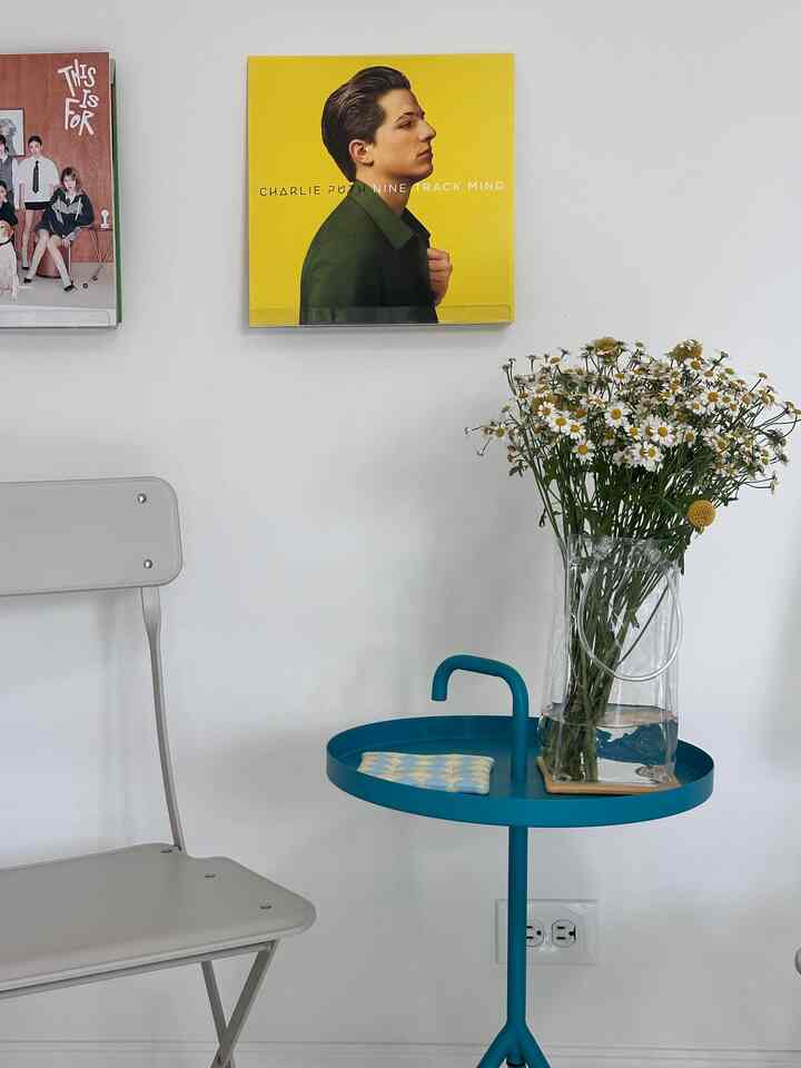 White-walled single seating space featuring a blue side table, vase, and framed wall art creating a cozy small music corner