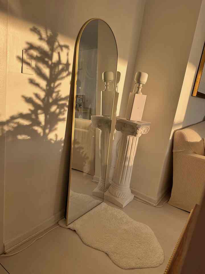 Soft white and ivory toned living room featuring an arched full-length mirror and classic Corinthian column pedestal, creating a romantic atmosphere