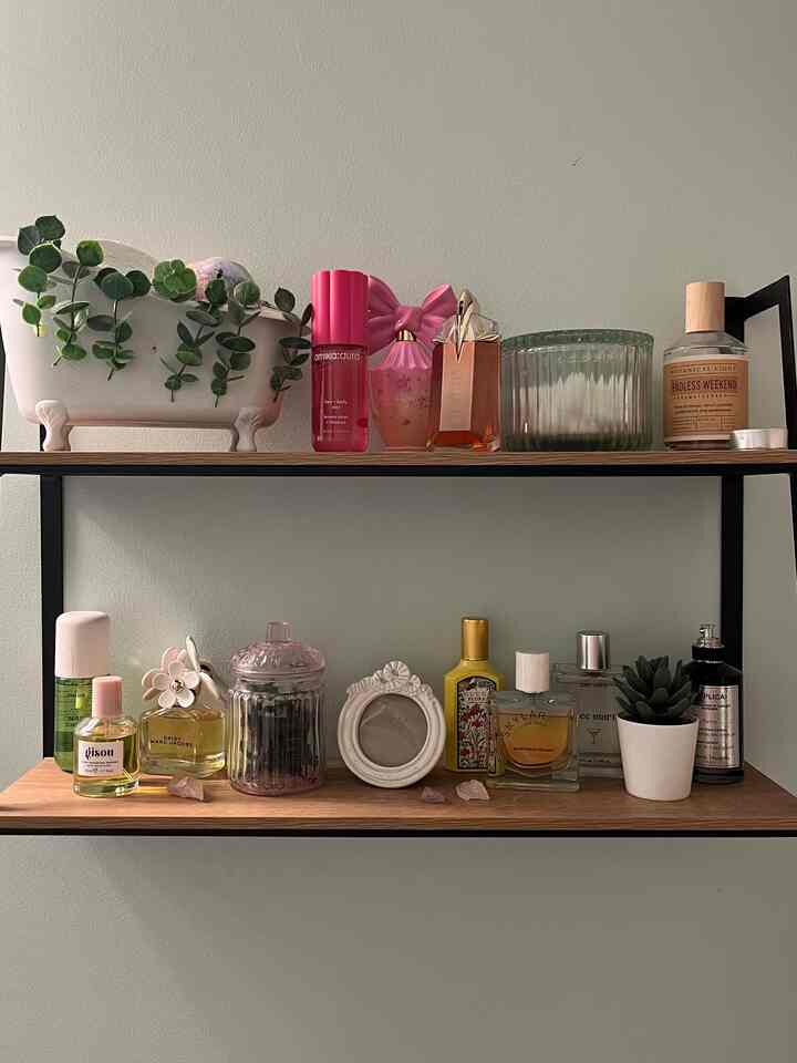 Wood-tone shelves against white wall in bathroom space, organized with various perfumes and plants as decor