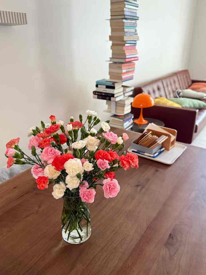 Mid-Century Modern living room with natural wood tone table featuring vibrant pink and white flowers in a vase