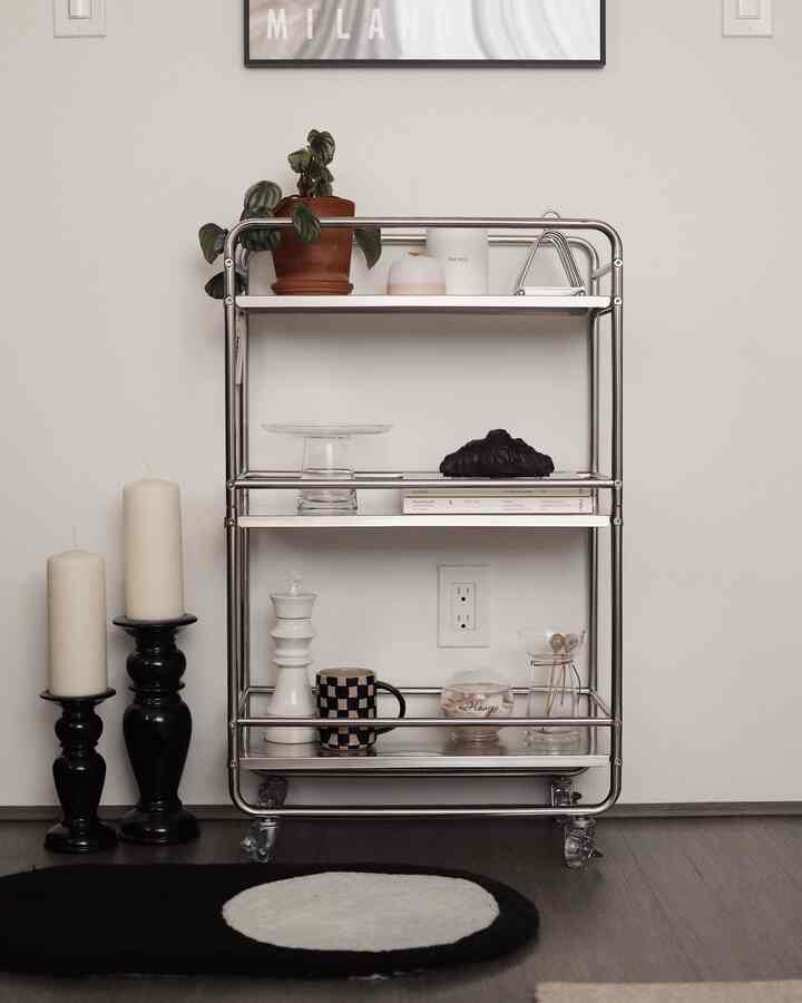 White and silver toned kitchen space featuring a mid-century modern metal shelf cart with surrounding candles and rug, creating a simple modern interior.