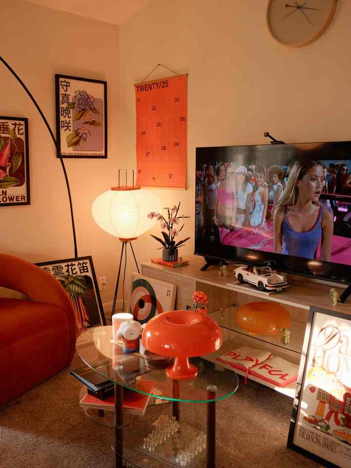 Warm orange-toned living room featuring glass coffee table, orange sofa, and paper floor lamp with a cozy atmosphere