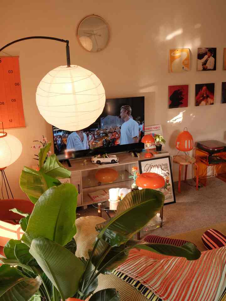 Orange-toned living room with natural lighting, featuring green plants, retro-style lamps, and wall art creating a cozy atmosphere