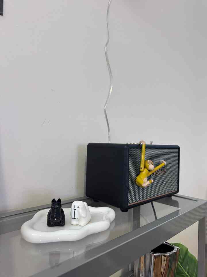 Simple space with a white wall and gray metal shelf holding a black radio and animal figurine objets