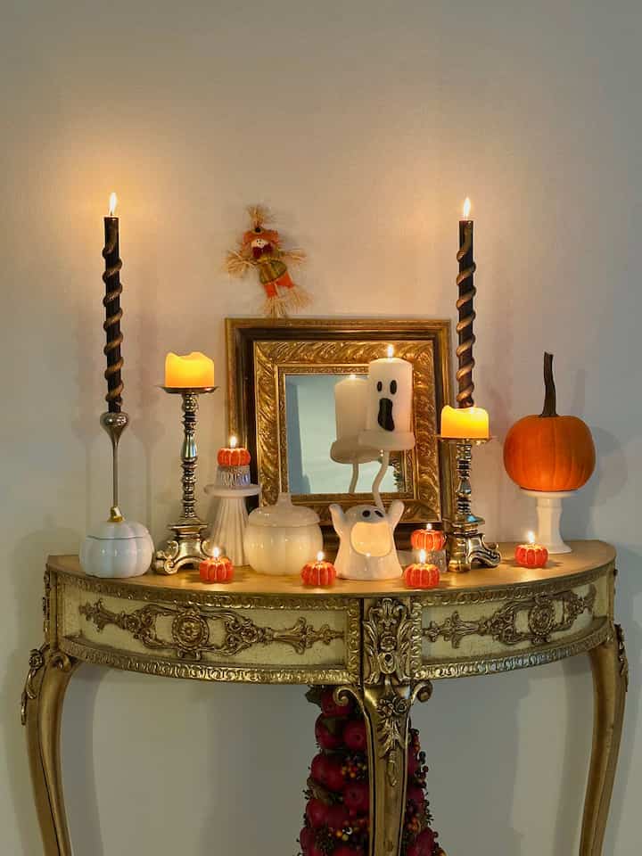 Warm orange and white-toned entrance featuring a French Country style gold console table and mirror adorned with Halloween candles and decorations creating cozy atmosphere