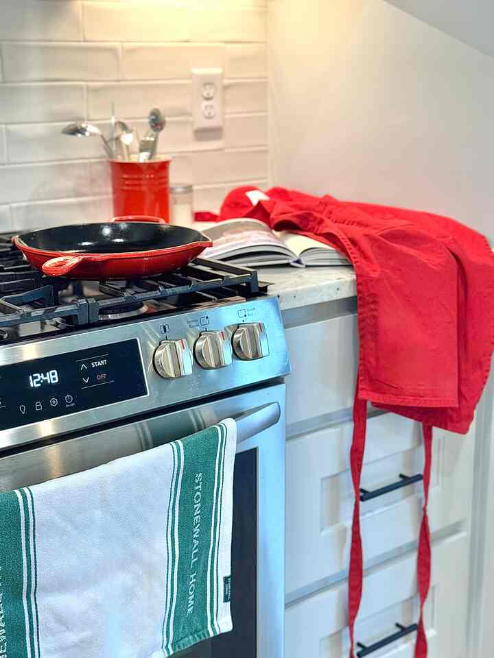 Kitchen with red and white tones featuring a red skillet on the stove, apron on the counter, and sleek tile backsplash