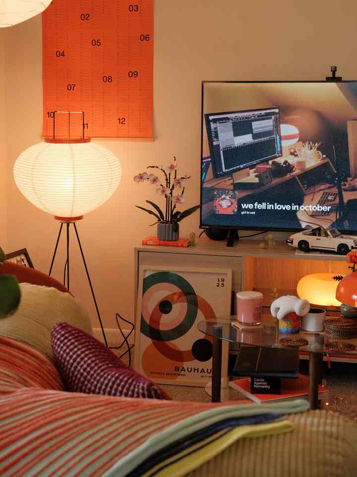 Orange and brown toned living room featuring a floor lamp, coffee table, posters with a warm home office and gallery atmosphere