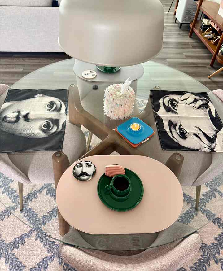 Natural-toned dining room featuring a round glass dining table with coffee cup, artistic coasters, and tissue case creating a modern home cafe vibe