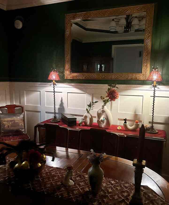 Dining room with dark green walls and beige vases, featuring classic wooden furniture and warm cozy autumn lighting