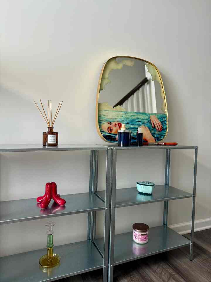 Silver metal shelves against white walls in an entrance space featuring a unique artistic mirror, diffuser, and candles creating a stylish interior