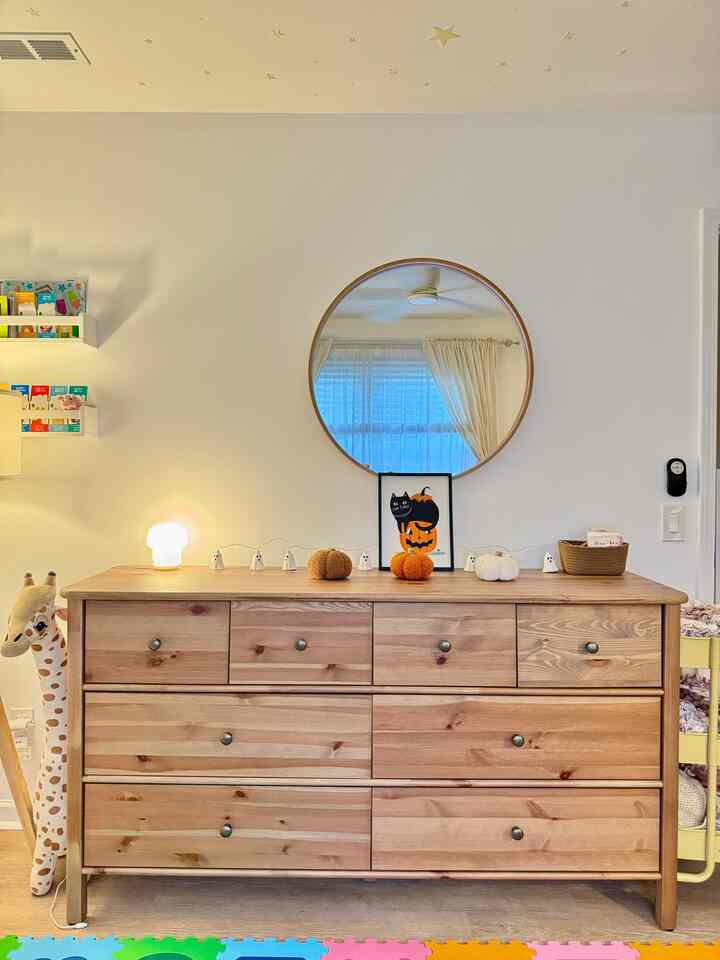 Natural color and white toned kids' room featuring wooden dresser and Halloween decorations in a cozy toddler play area