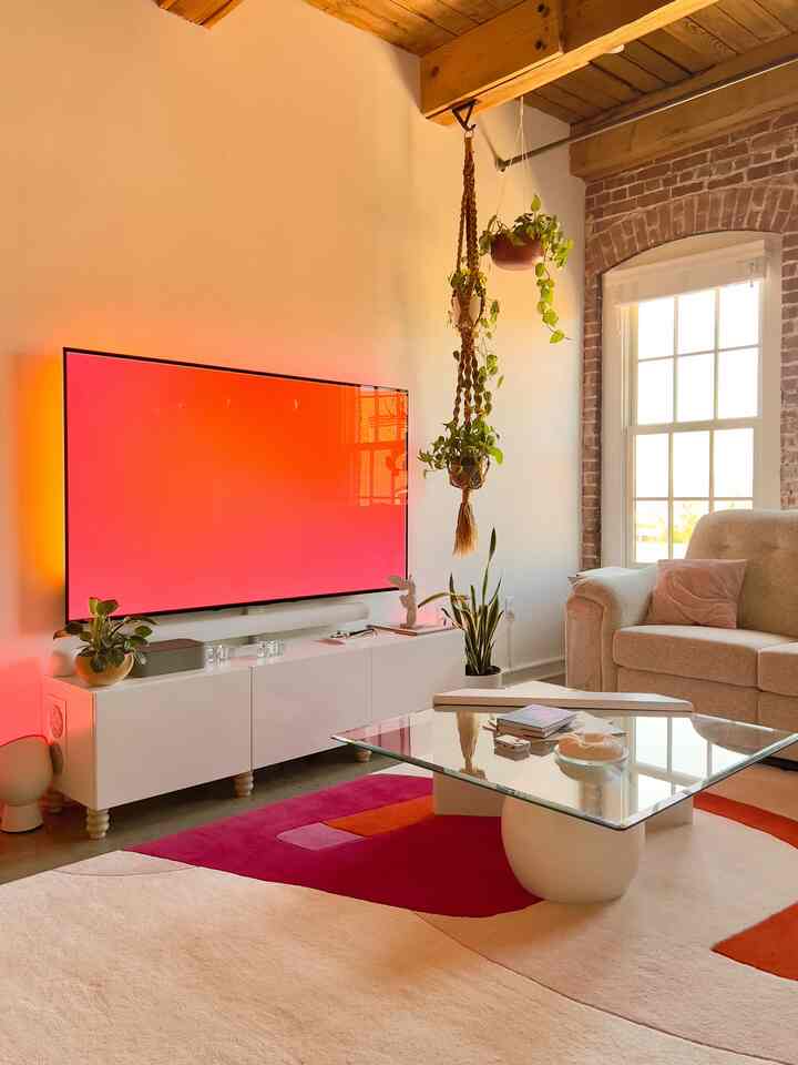 Talk about a mood! 💖 This living room transforms at night with those vibrant LED lights behind the TV. And that rug? A serious statement piece! Such a playful and chic space. ✨📺🌿 #LivingRoomGoals #LEDLighting #AmbientLighting #HomeDecor #StatementRug #PinkAndOrange #ModernLiving #CozyNights 