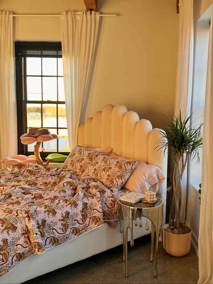 Warm beige and white toned bedroom featuring a velvet bed with scalloped headboard and flower-shaped cat tower, bathed in sunlight for a cozy atmosphere