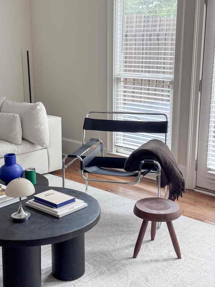 Bright and calm living room with white walls and sofa, featuring modern mid-century armchair and wooden stool