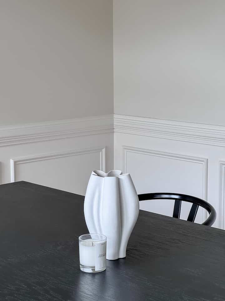 Modern dining space with white and black tones featuring a dining table and chair, centered white ceramic vase and candle on the table