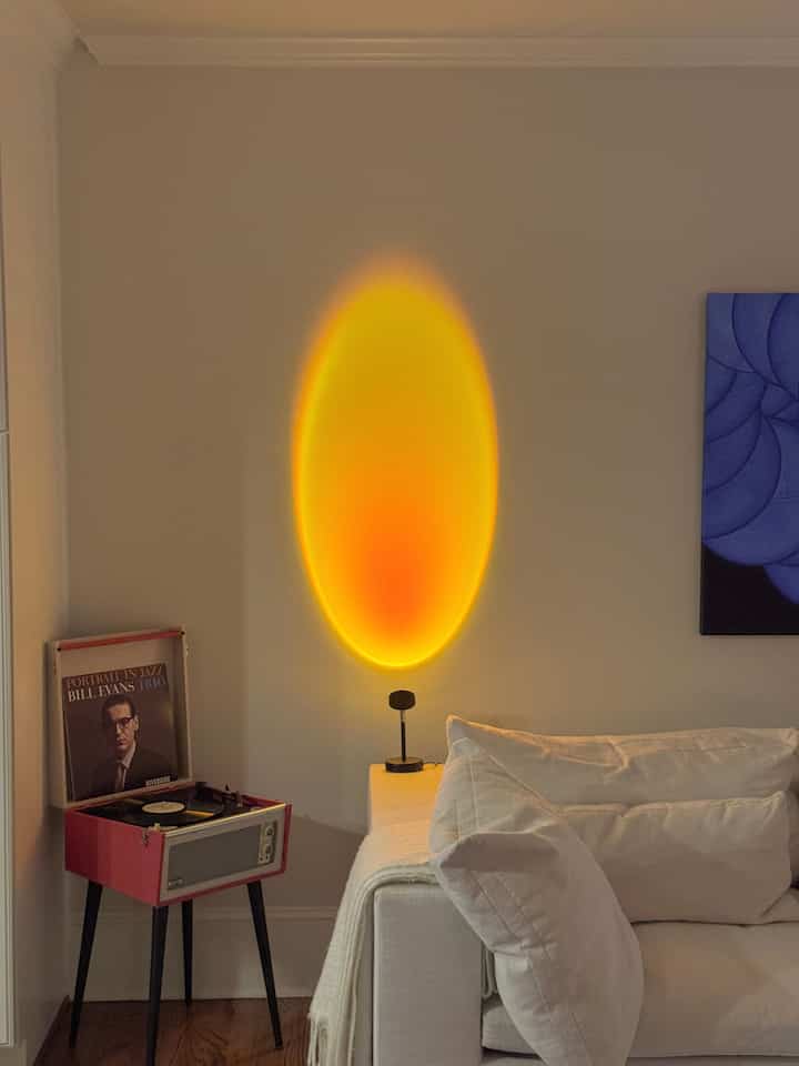 Living room in warm rose gold and white tones featuring a sofa, record player, and ambient sunset lamp creating a cozy atmosphere