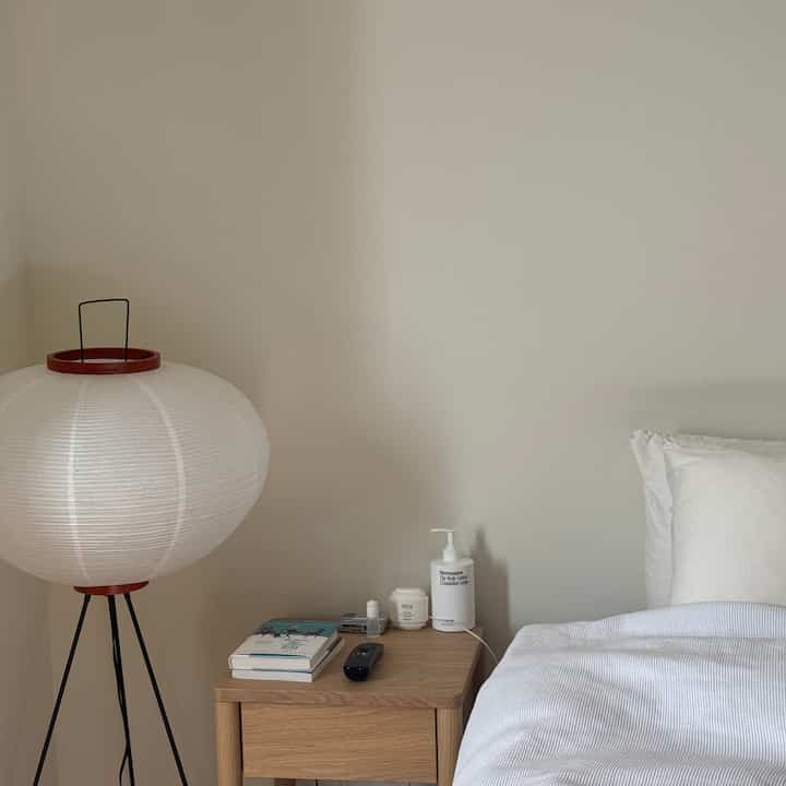 Soft white and wood toned bedroom featuring a nightstand and floor lamp in a cozy Japandi style setting