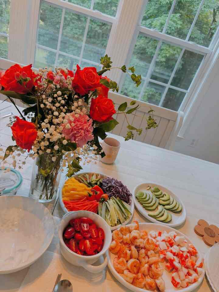 White-toned dining room featuring fresh vegetables and red rose vase on a clean, natural meal setting