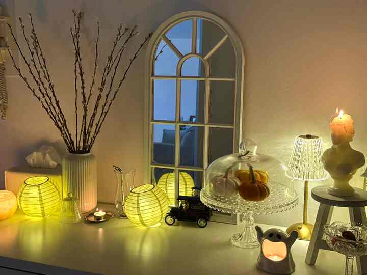 Warm entrance area with soft yellow lighting, featuring a vase with branches, paper lanterns, and mini pumpkins on a glass cake stand creating a cozy fall vibe
