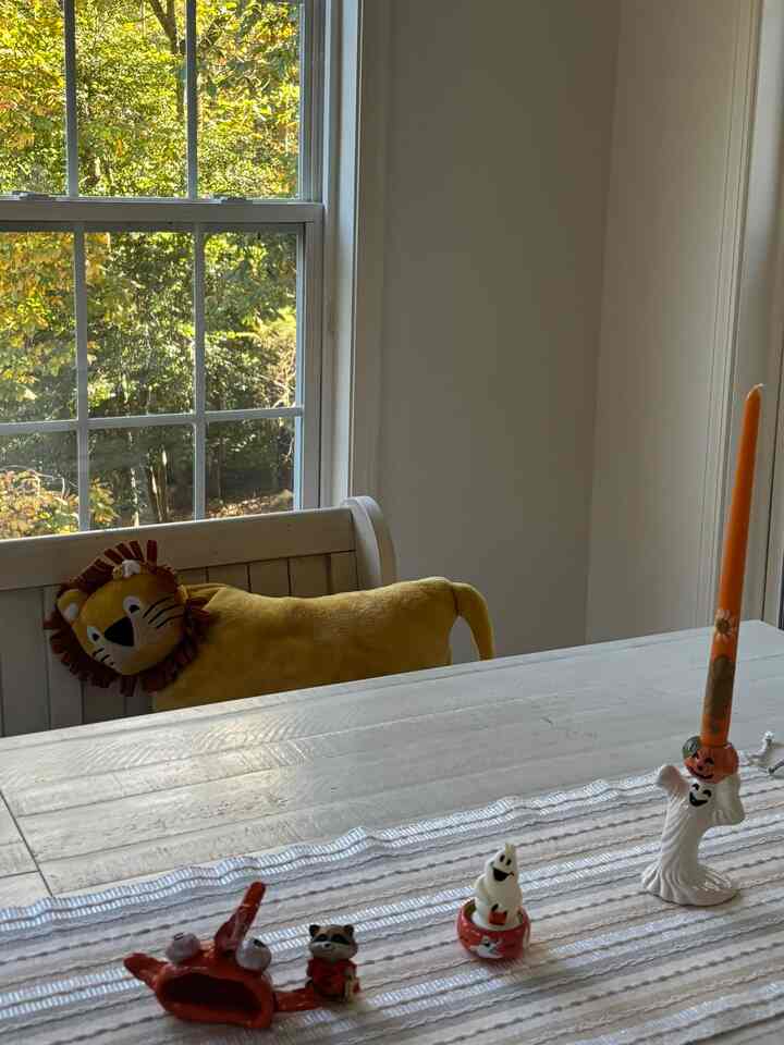 Warm beige dining room featuring a window-side bench with a yellow lion cushion and autumn-themed candles creating a cozy atmosphere